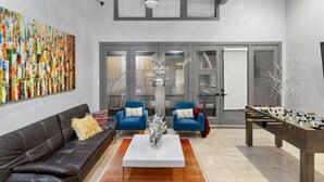 A modern living room with a sofa, two armchairs, a coffee table, and a foosball table.