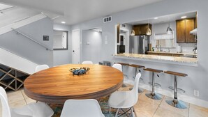A modern kitchen with a central island, bar stools, and a dining area with a round table and chairs.