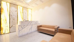 A reception area with a marble reception desk, a beige sofa, and a modern ceiling design. - Hotel Bonito- Delhi IGI Airport (New Delhi)