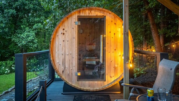 Estructura de sauna de madera con puerta de vidrio, rodeada por una terraza e iluminación exterior.