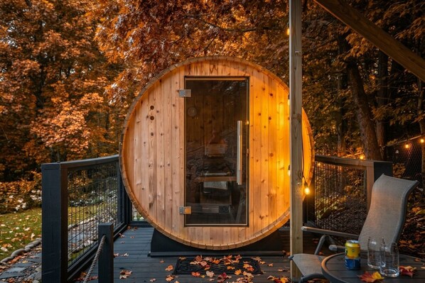 A wooden cabin with a glass door, a deck with a chair and table, and a forested background.