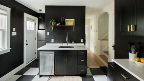 Cozinha moderna com armários pretos, bancadas brancas e chão quadriculado em preto e branco.