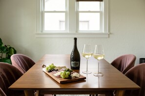 A wooden table with a bottle of wine, two glasses of wine, and a charcuterie board with grapes, olives, and cheese.