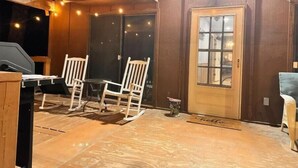 Un espace extérieur accueillant avec des chaises et une table en bois, une porte en bois dotée d’un panneau de verre et des guirlandes lumineuses.