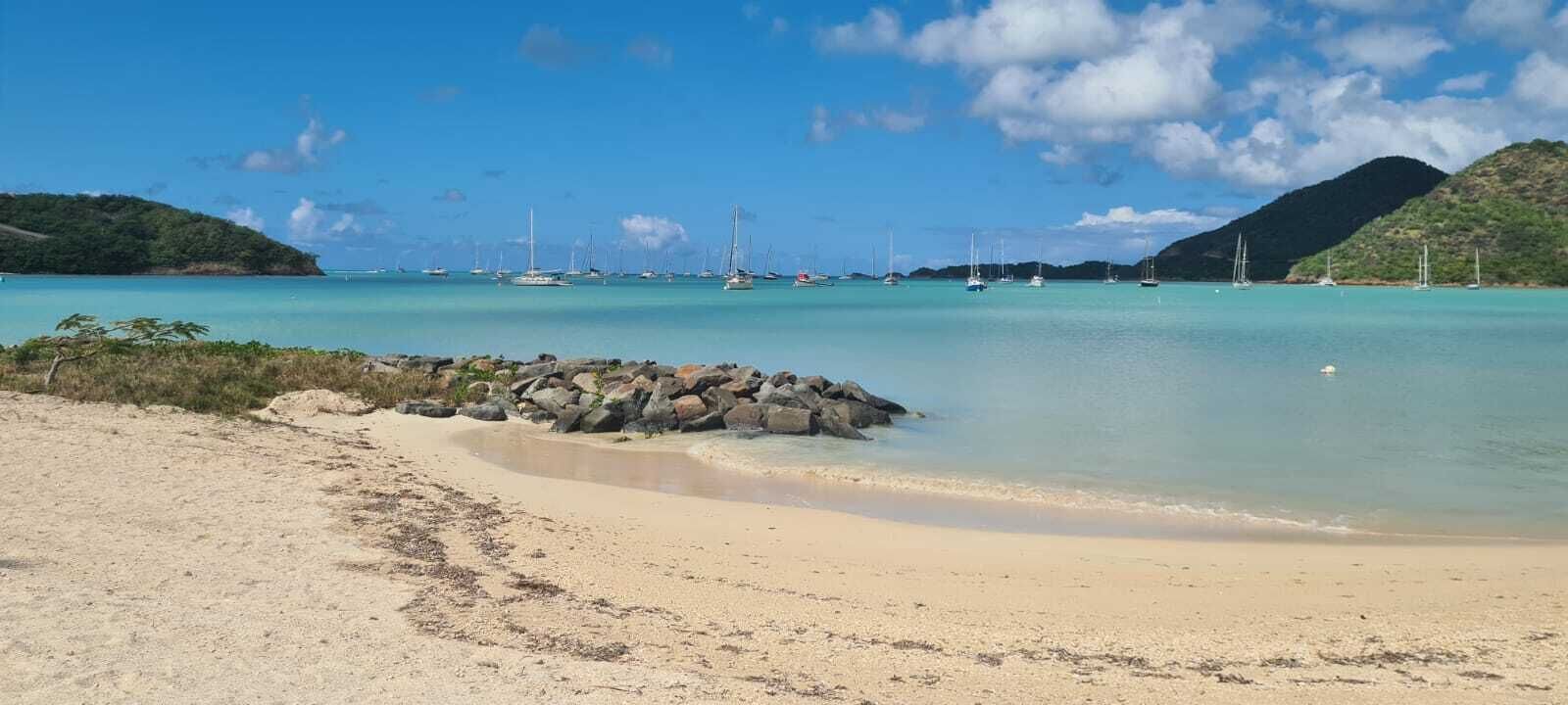 A beach with clear turquoise water, a rocky breakwater, and a distant bridge.