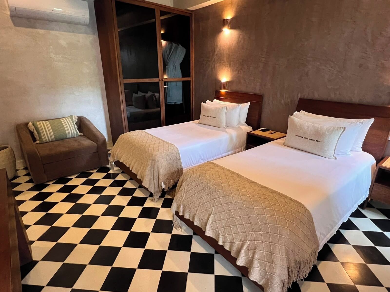 A hotel room with two beds, a checkered floor, a sofa, and a wardrobe.