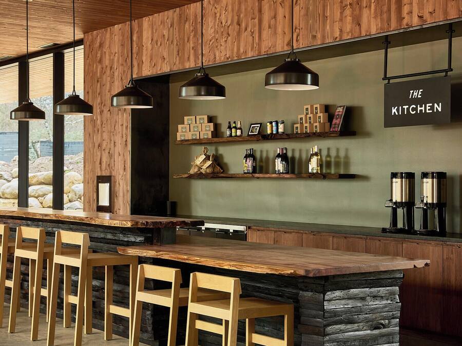 A modern kitchen with a wooden island, bar stools, hanging pendant lights, and a sign reading "THE KITCHEN".