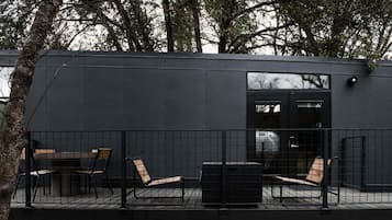 Un edificio moderno con fachada oscura, un patio amurallado con mobiliario y una puerta visible.