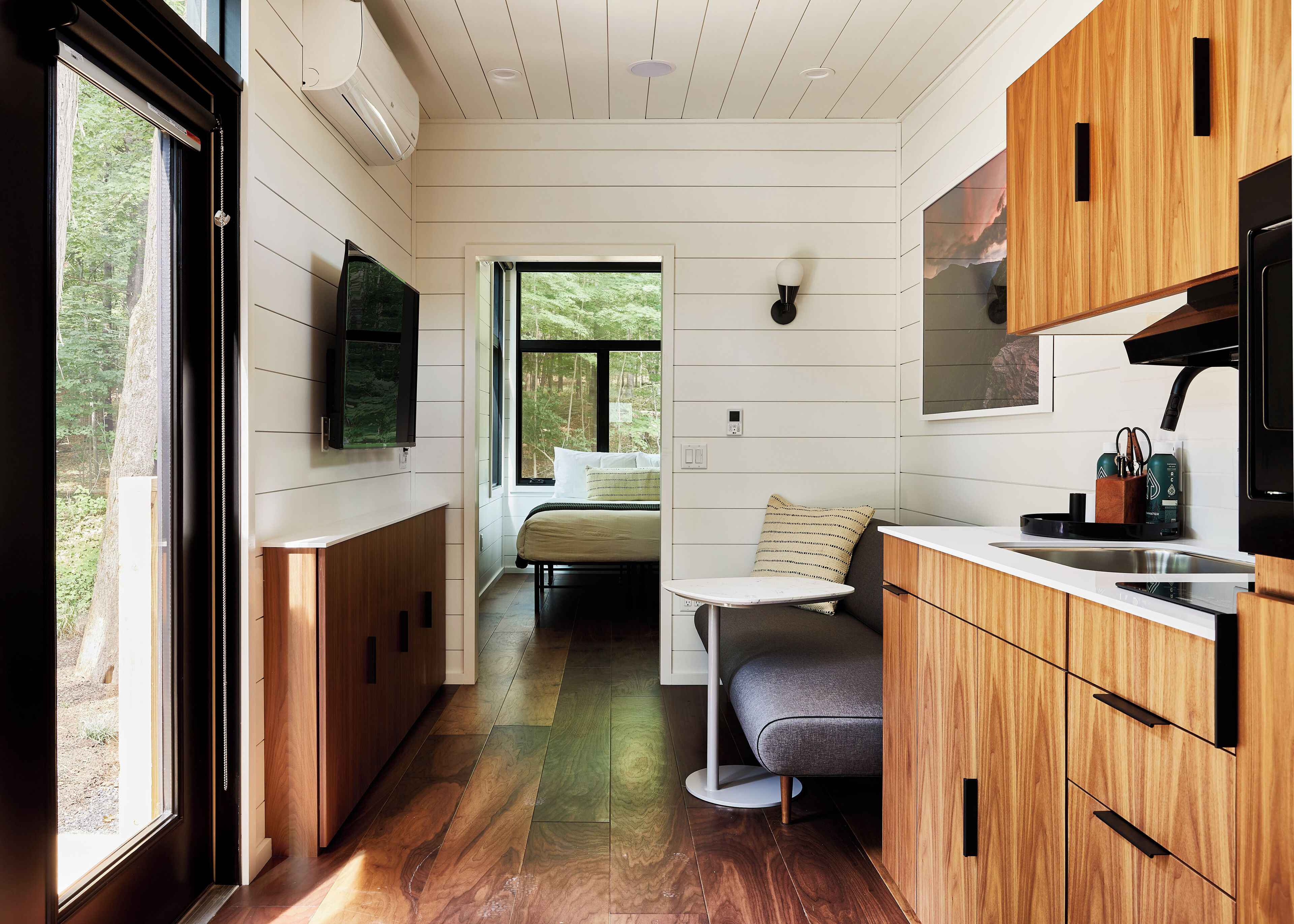 A compact kitchen with wooden cabinets, a built-in stove, and a window overlooking a forest.