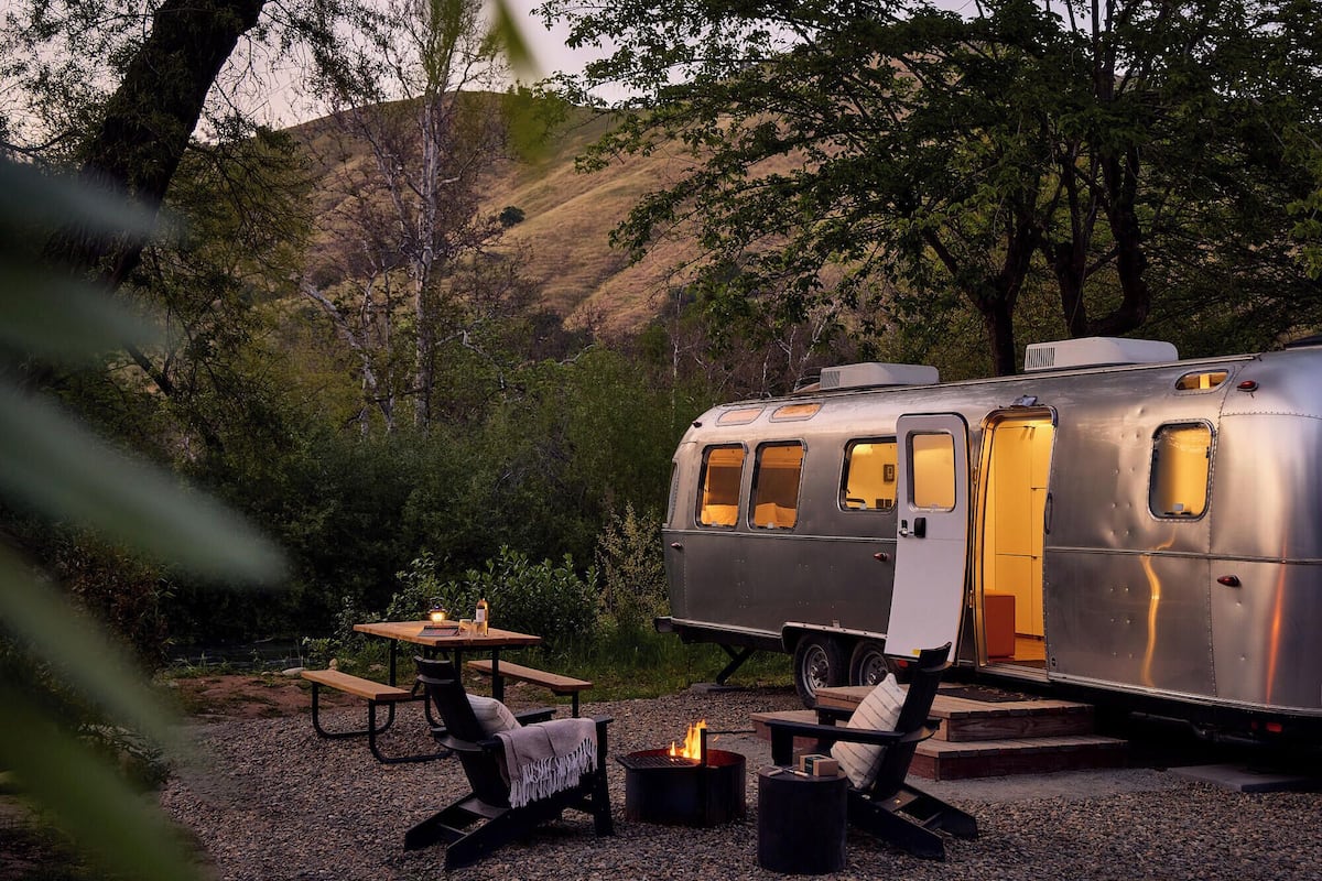 Una caravana antigua con una mesa y sillas dispuestas en un entorno natural.
