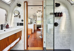 A modern bathroom with a glass shower enclosure, a vanity with a mirror, and a small seating area.