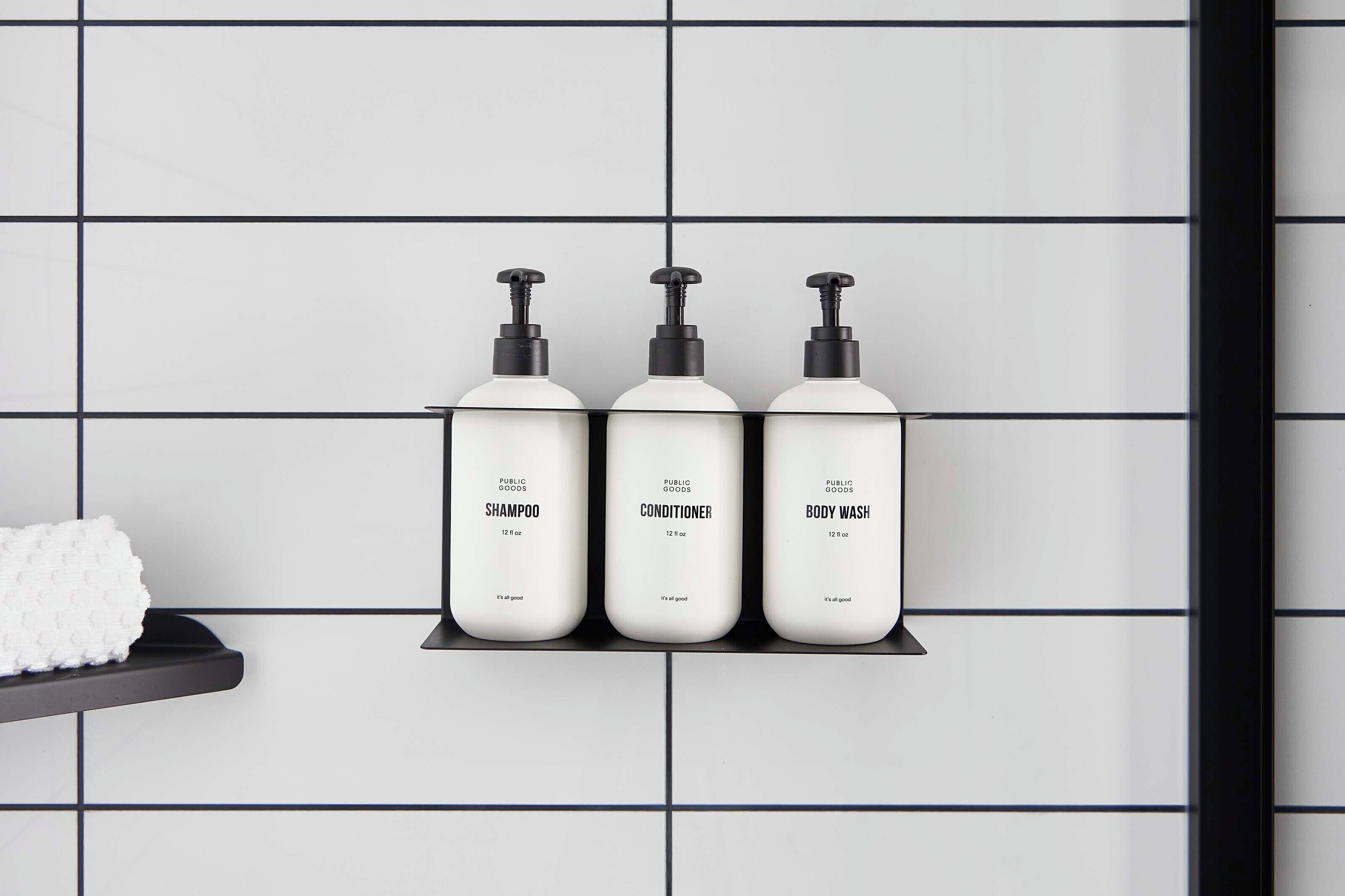 Three bottles of shampoo, conditioner, and body wash on a black shelf against a tiled wall.