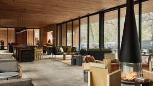A spacious living area with a large fireplace, wooden furniture, and large windows offering views of the outdoors. - AutoCamp Sequoia (Three Rivers)