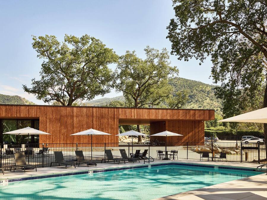 A modern outdoor pool area with lounge chairs and umbrellas, surrounded by a wooden fence and trees.