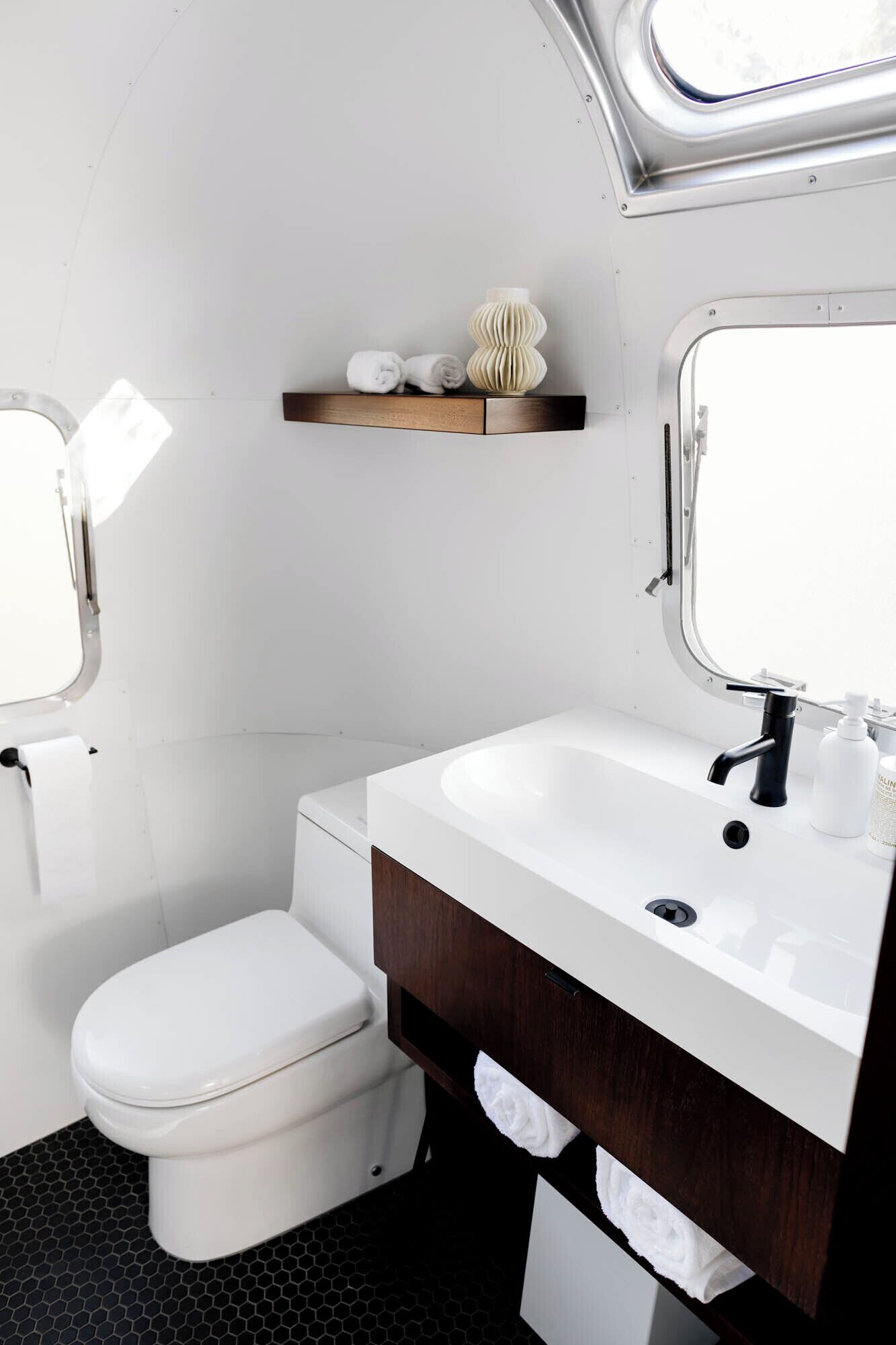 A compact bathroom with a white toilet, a wooden vanity with a white sink, and a mirror above the sink.
