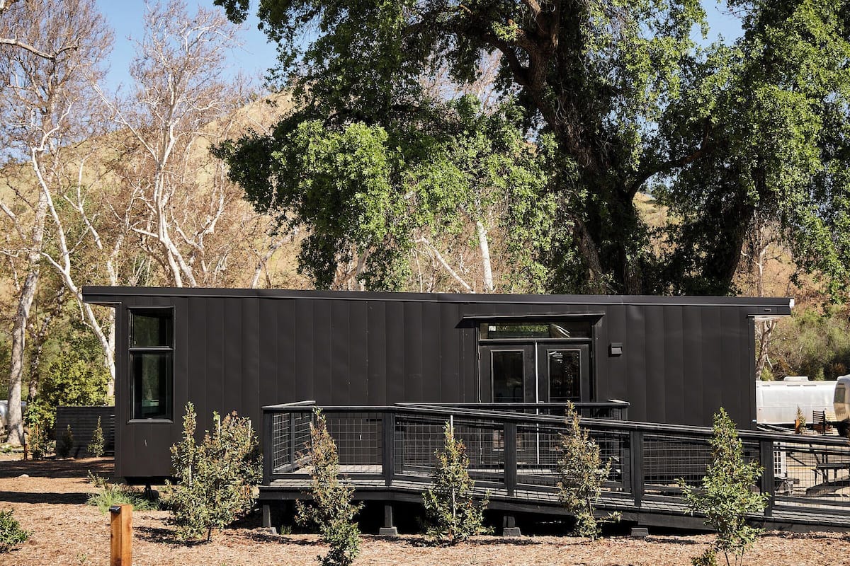 Una cabaña moderna de color oscuro con una pequeña terraza y un acceso cubierto.