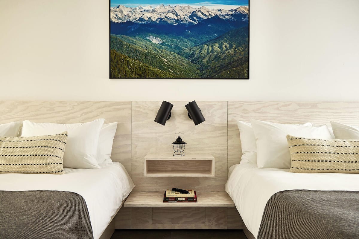 Habitación de hotel con dos camas, una mesita de noche con un farol y vistas a la montaña.