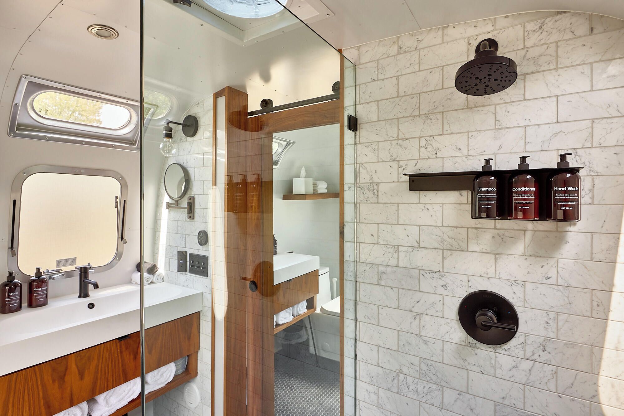 Et moderne badeværelse med en glasbrusekabine, et vaskeskab med spejl og en vægmonteret hylde med toiletartikler.