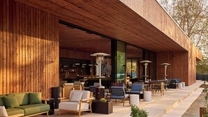 An outdoor seating area with wooden furniture and a modern building facade. - AutoCamp Sequoia (Three Rivers)