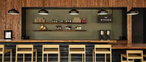 A bar area with wooden chairs, shelves with bottles, and a sign reading "THE KITCHEN".