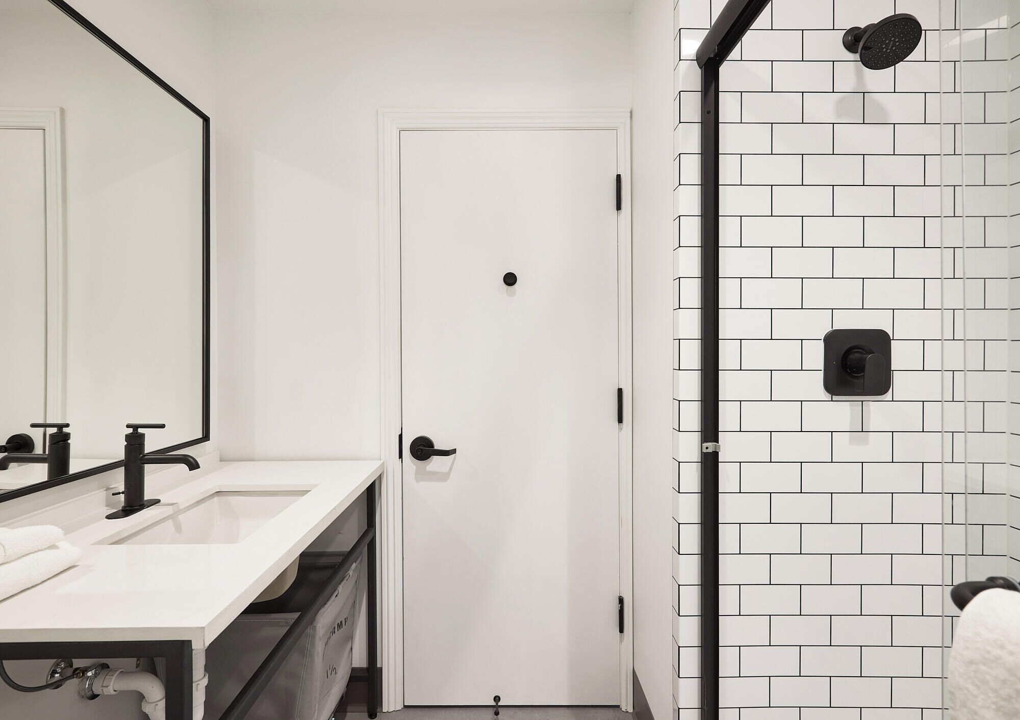 A bathroom with a white door, a sink with a mirror, and a shower with a black faucet.