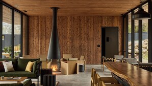 A modern interior with a central wood-burning stove, comfortable seating, and large windows offering views of the outdoors. - AutoCamp Sequoia (Three Rivers)