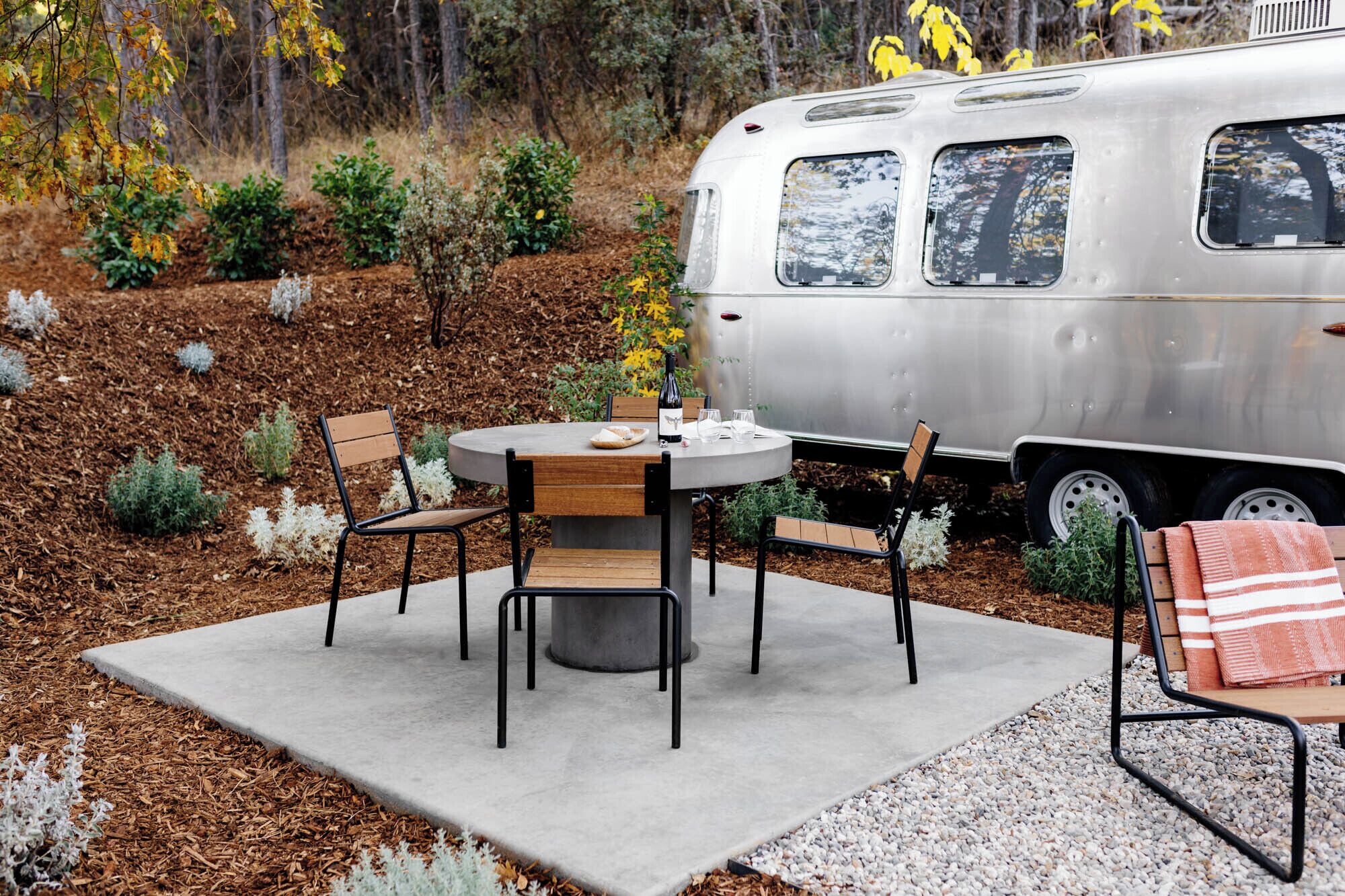 An outdoor seating area with a round table and chairs, a concrete floor, and a small rug.
