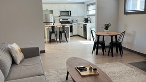 A modern living room with a grey sofa, a wooden coffee table, and a dining area with a round table and chairs. - East Rock Inn (Great Barrington)