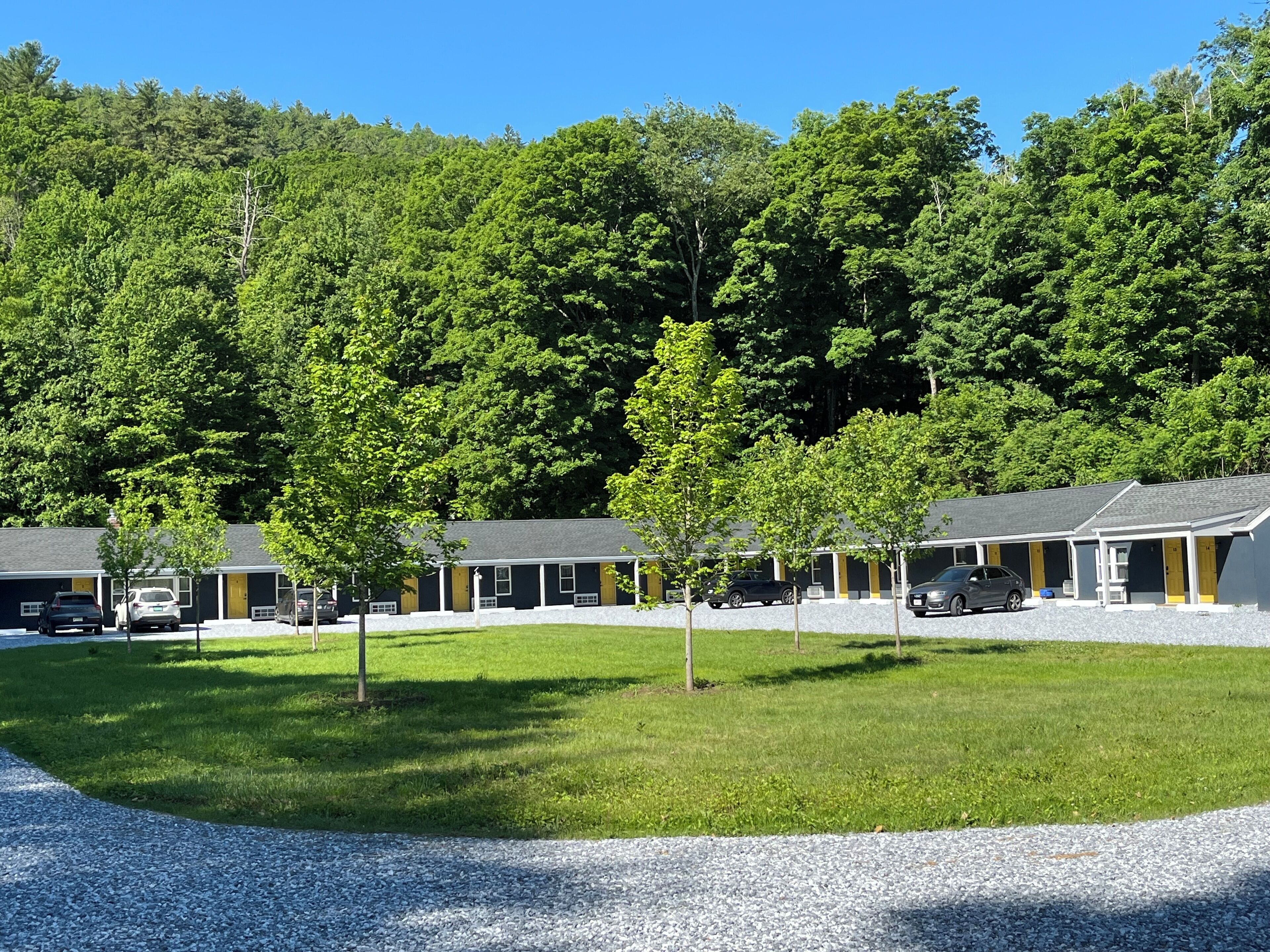 Un motel con varias habitaciones, un camino de grava y un fondo de bosque.