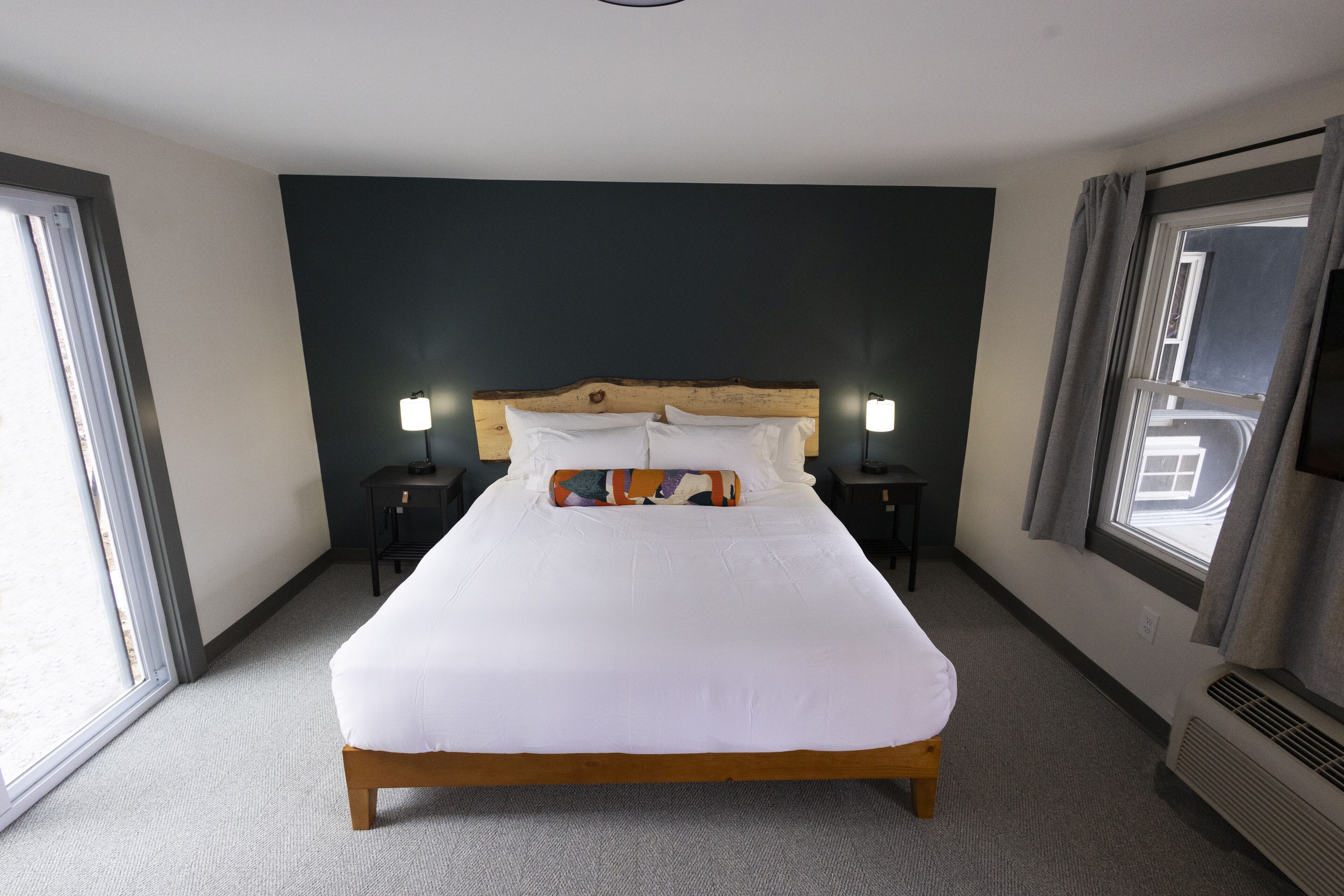 Habitación de hotel con una cama grande, dos mesitas de noche, cabecero y una ventana con cortinas.