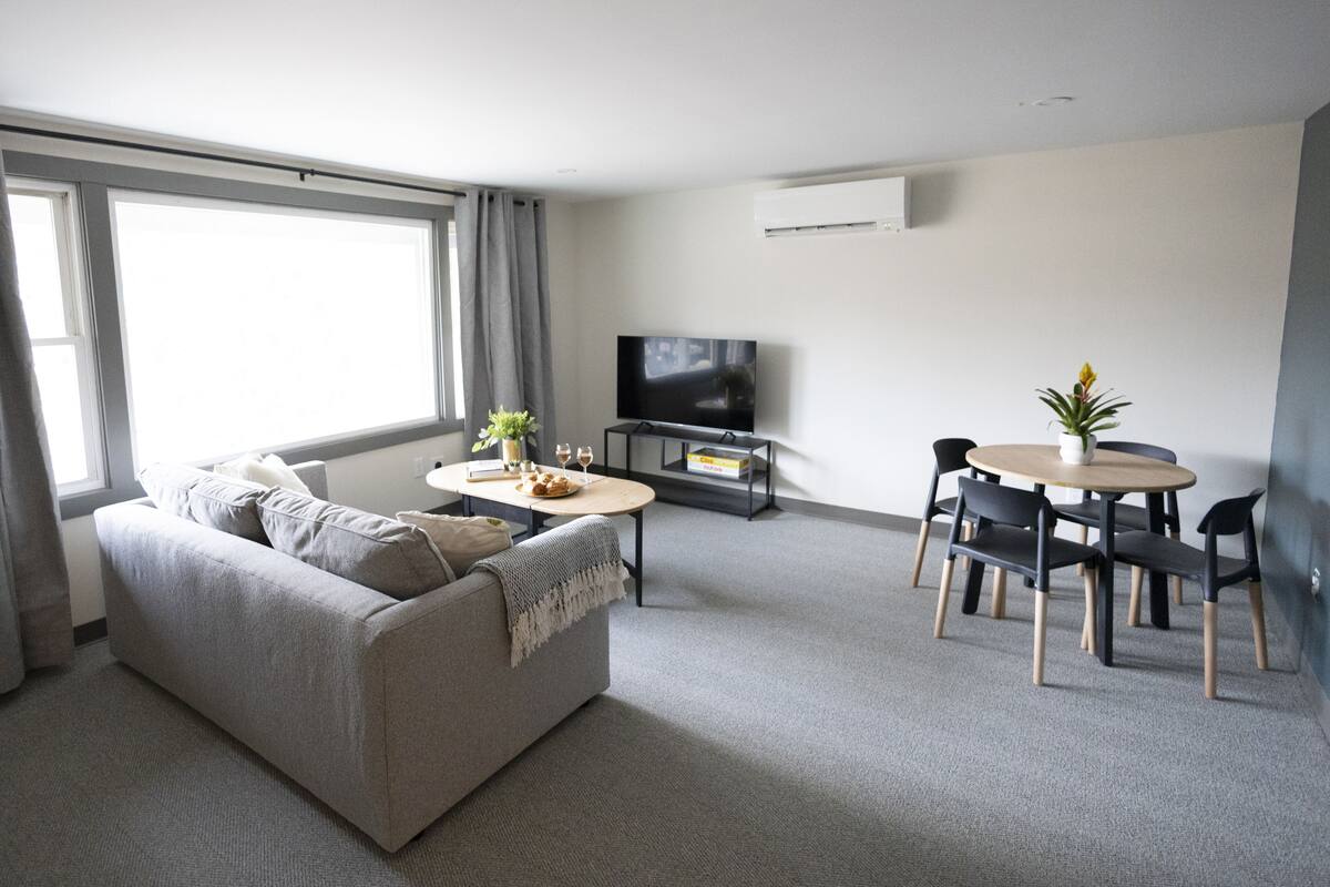 Una sala de estar moderna con un sofá, un televisor, una mesa de comedor con sillas y una planta pequeña.