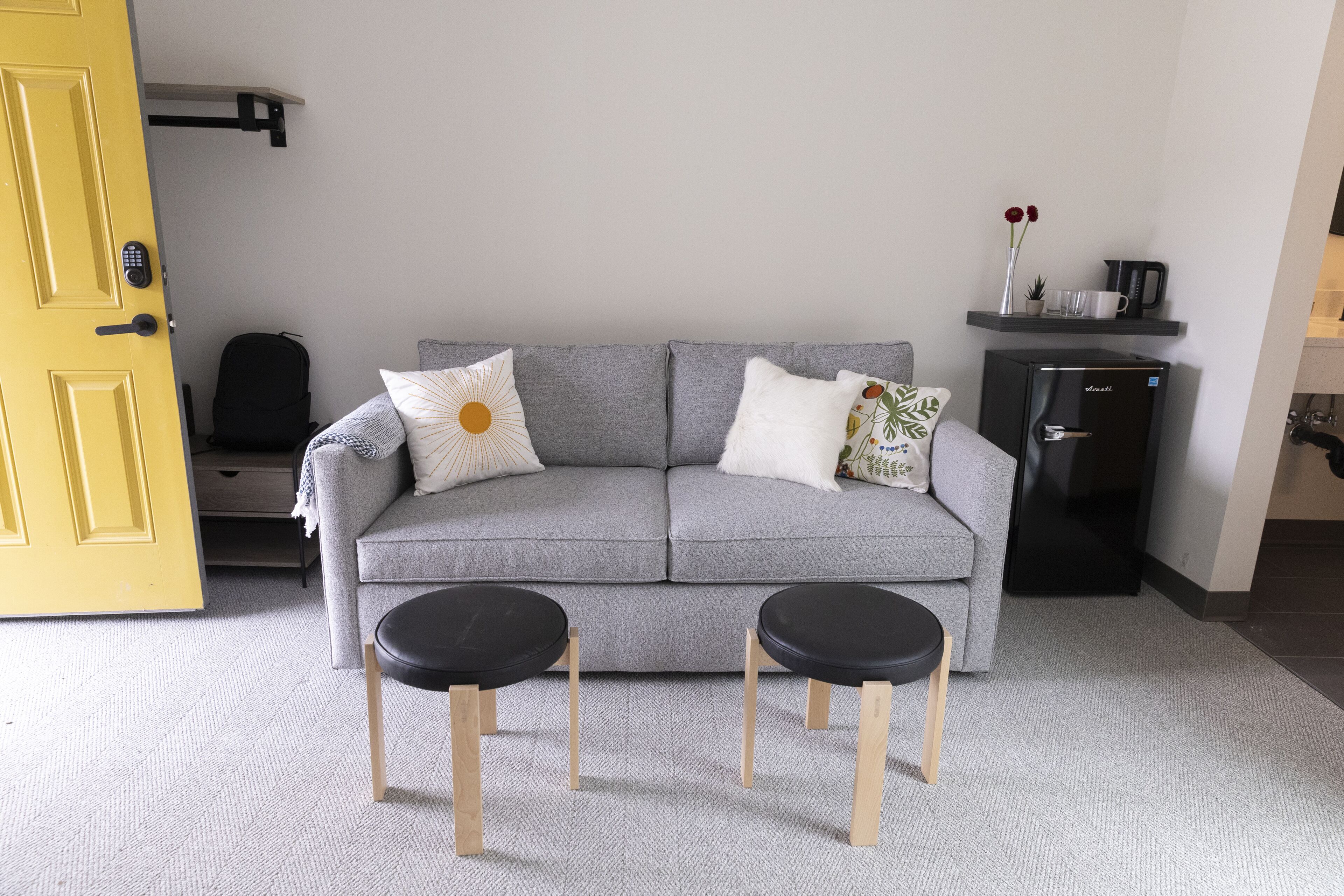 A modern living room with a grey sofa, two black side tables, and a small black coffee machine on a shelf.