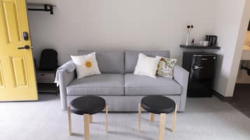 A modern living room with a grey sofa, two black side tables, and a small black coffee machine on a shelf.