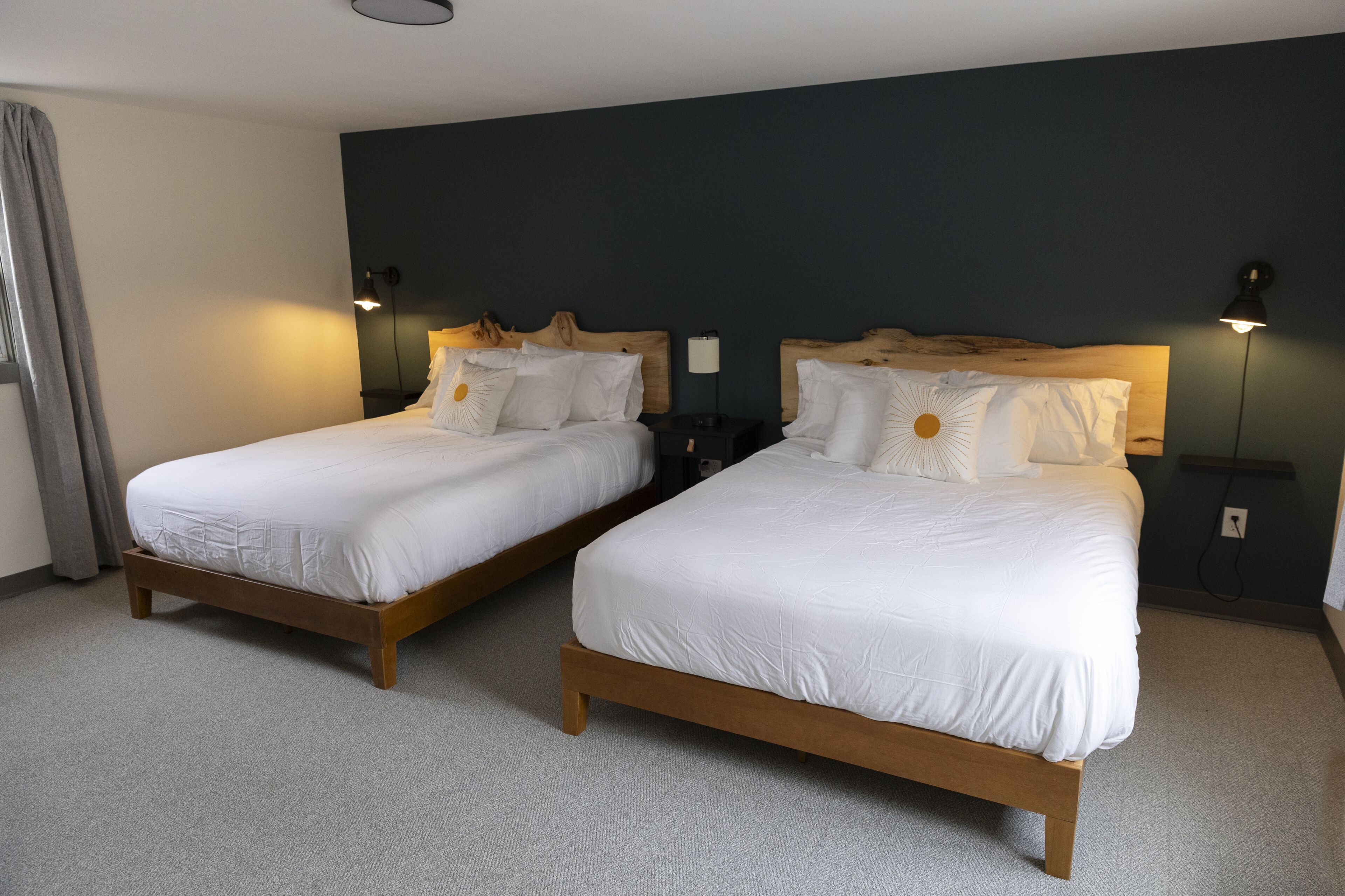 Two single beds with wooden frames and white bedding, a dark wall, and a light-colored carpet.