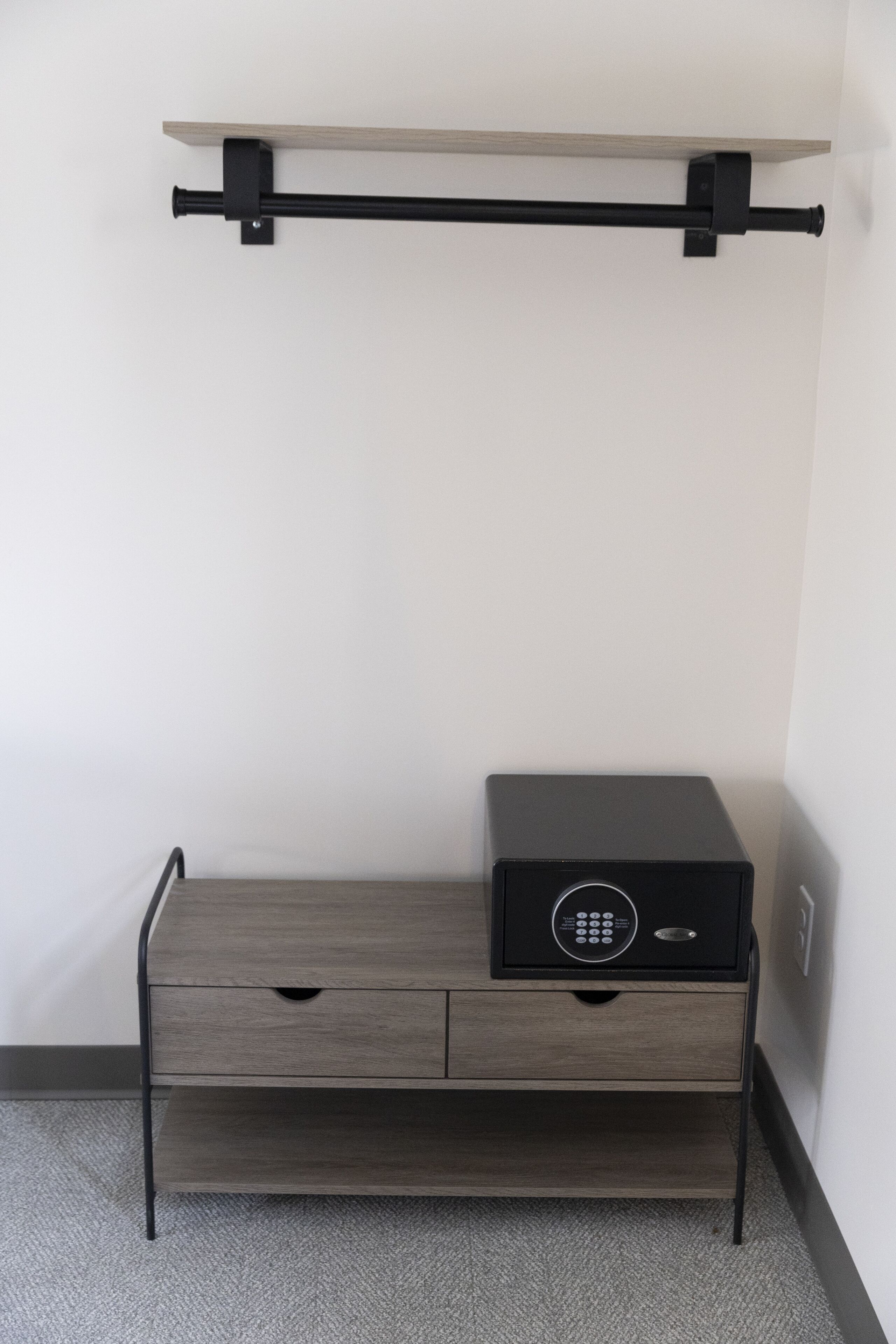 Habitación compacta y moderna con diseño minimalista, que incluye un estante de madera, un mueble negro con cerradura incorporada y una cómoda de madera.