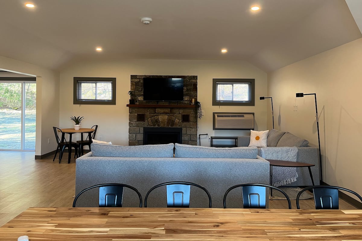 Amplia sala de estar con chimenea de piedra, un televisor de pantalla plana montado encima, un sofá y una mesa de comedor con sillas.