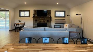 A spacious living area with a stone fireplace, a flat-screen TV mounted above it, a sofa, and a dining table with chairs.