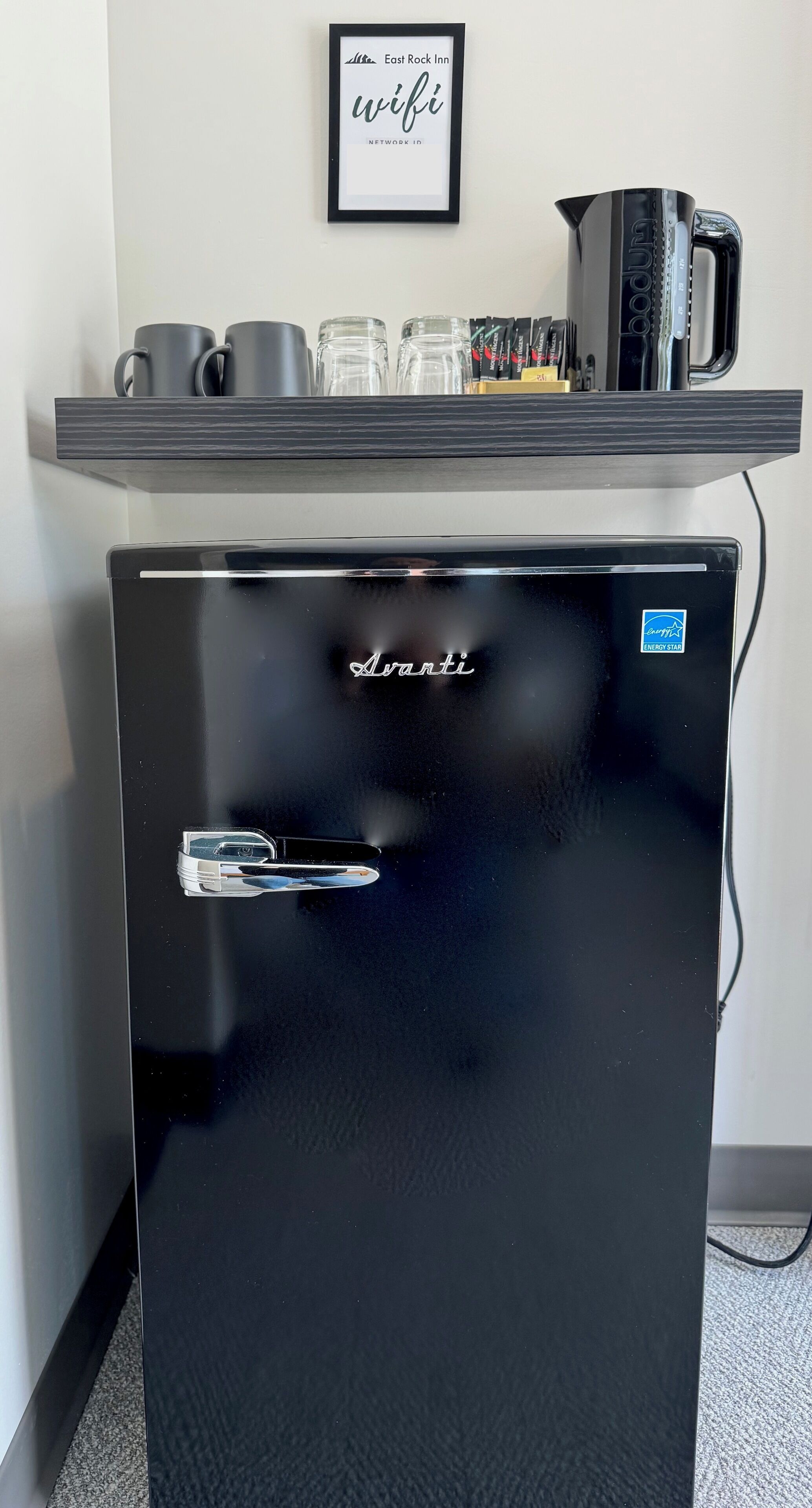 A black minibar with a logo, a coffee machine, and a framed sign above it.