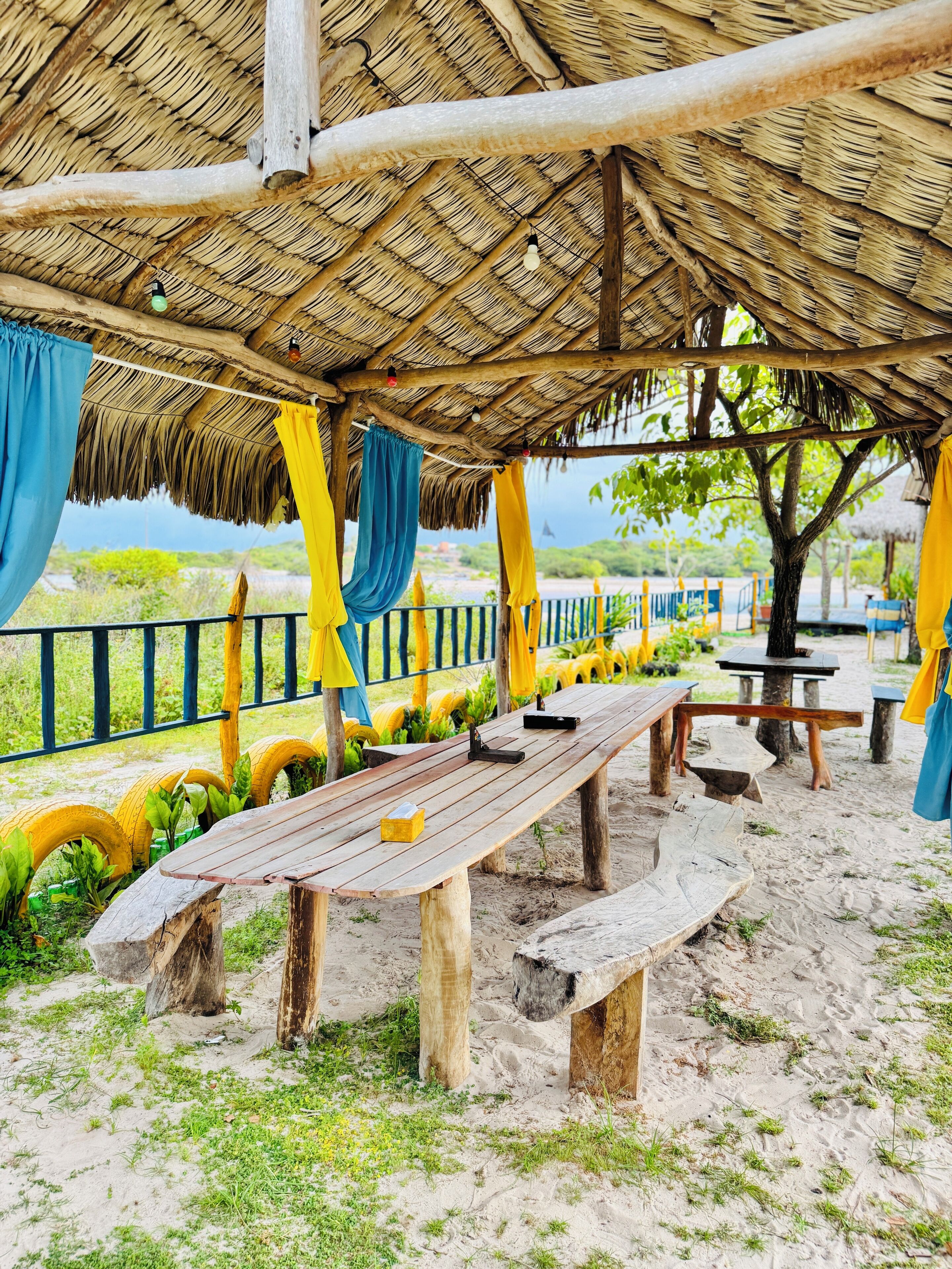 A beachside pavilion with a thatched roof, wooden benches, and a view of the sea.