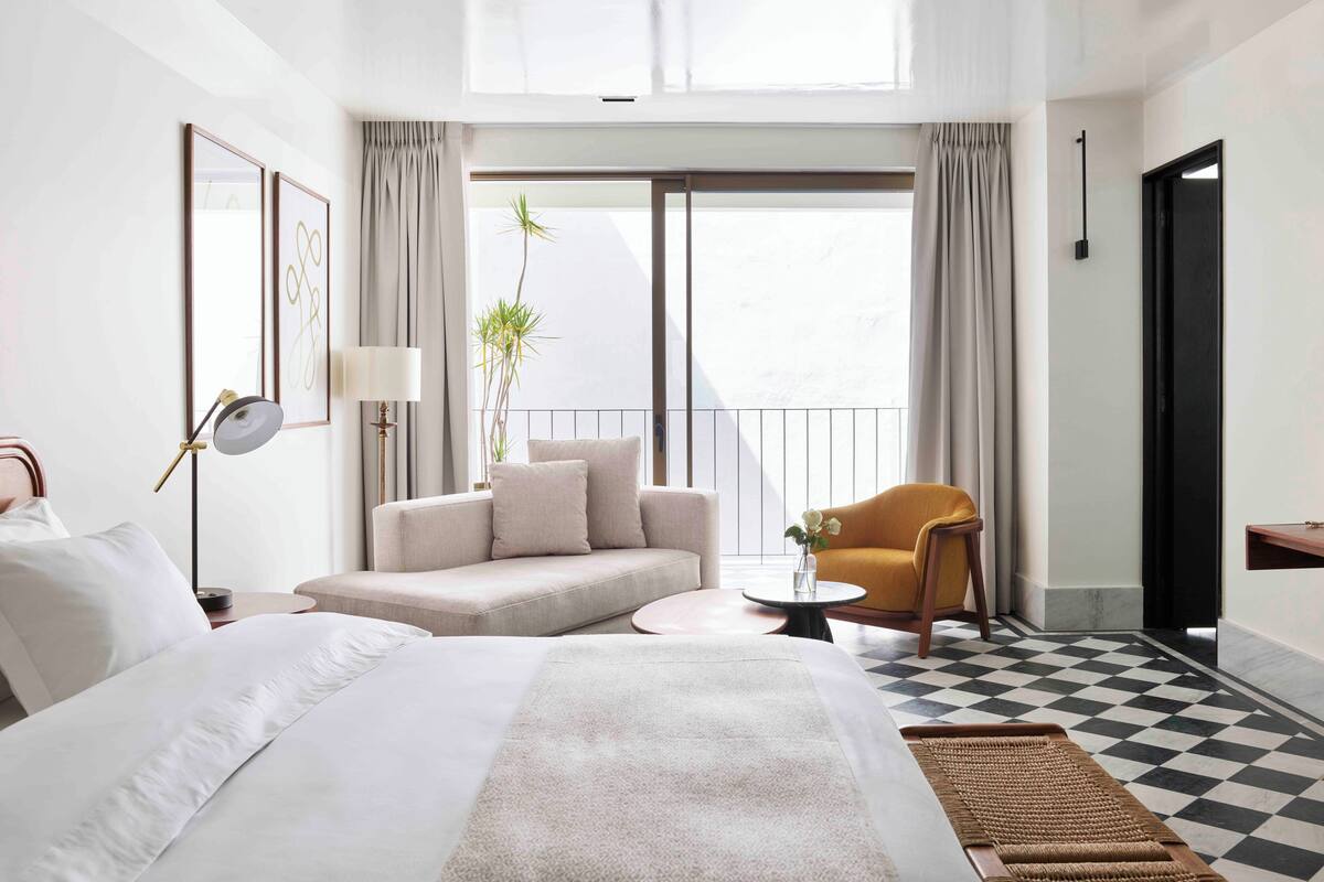 A hotel room with a bed, a sofa, a chair, a small table, and a balcony with curtains.