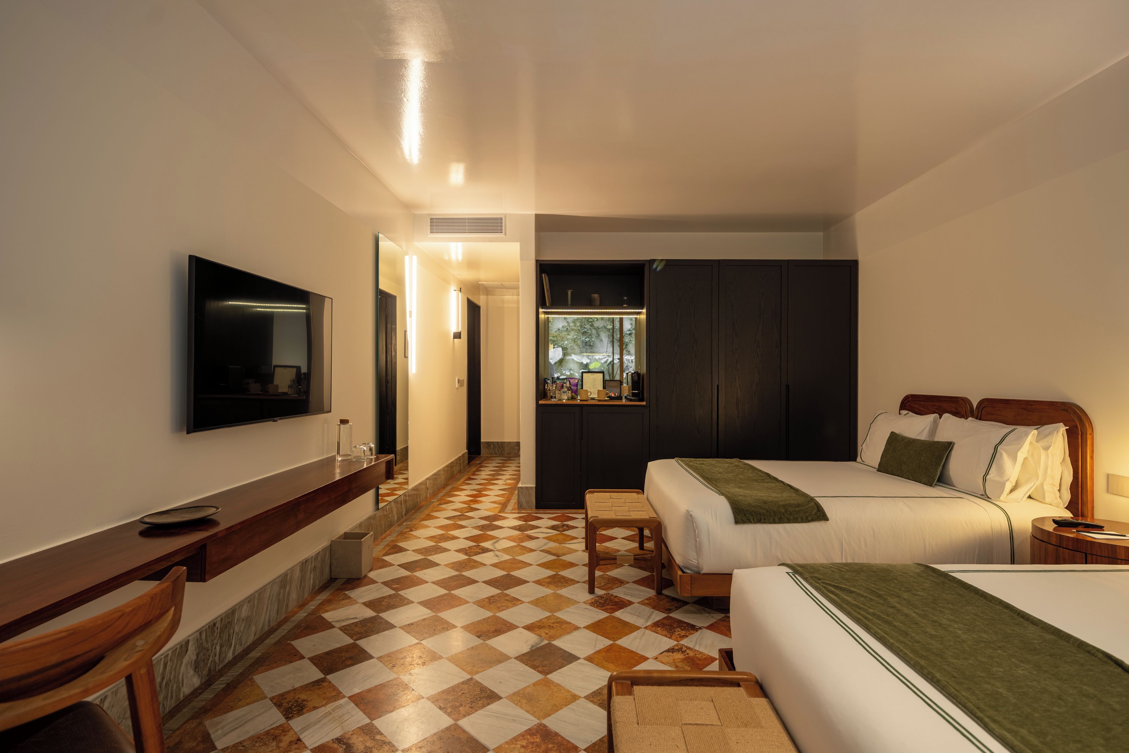 Una habitación de hotel con cama, mesita de noche, televisión y piso a cuadros.