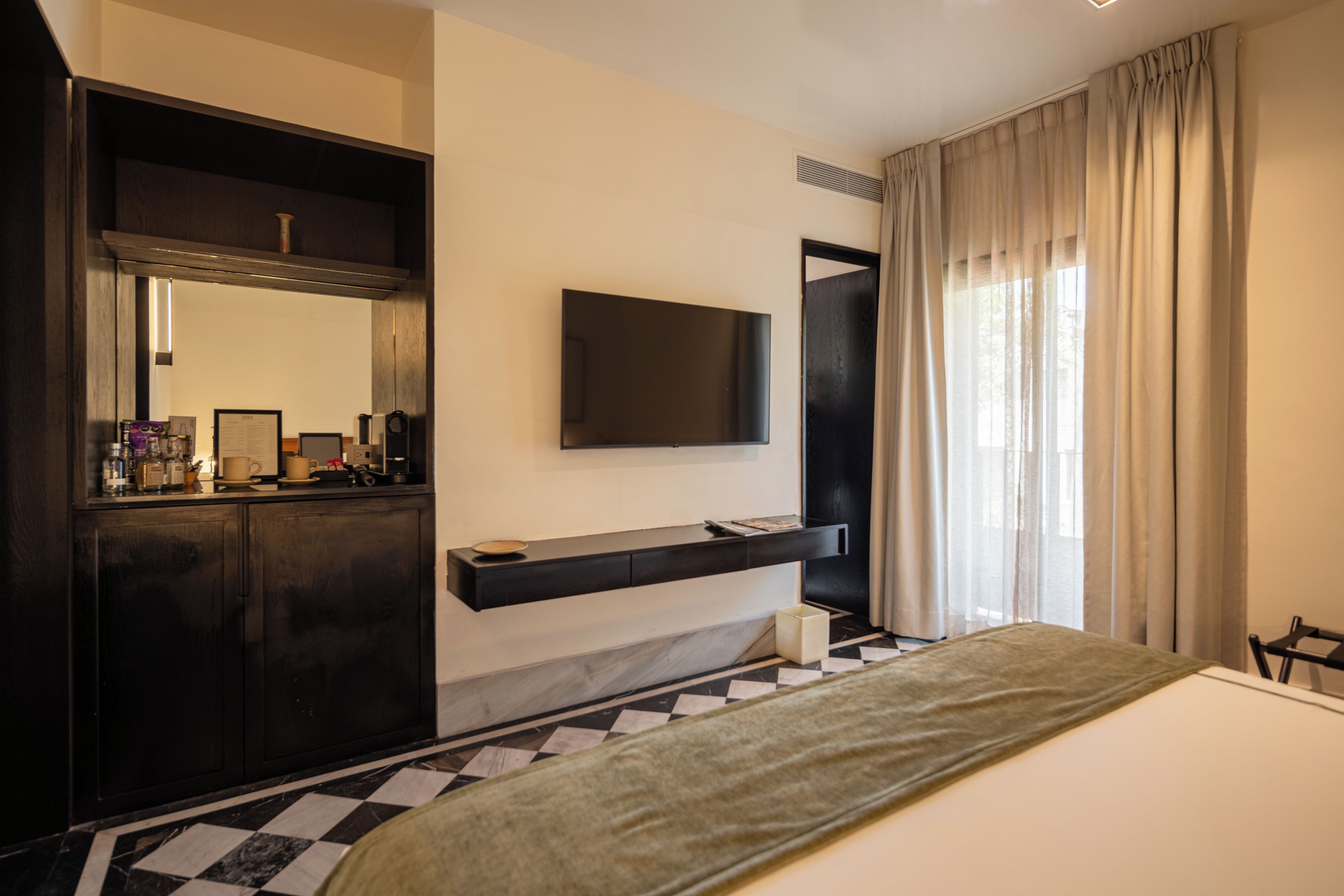 Ein Hotelzimmer mit einem Bett, einem an der Wand befestigten Fernseher, einem dunklen Holzschrank und einem karierten Boden.