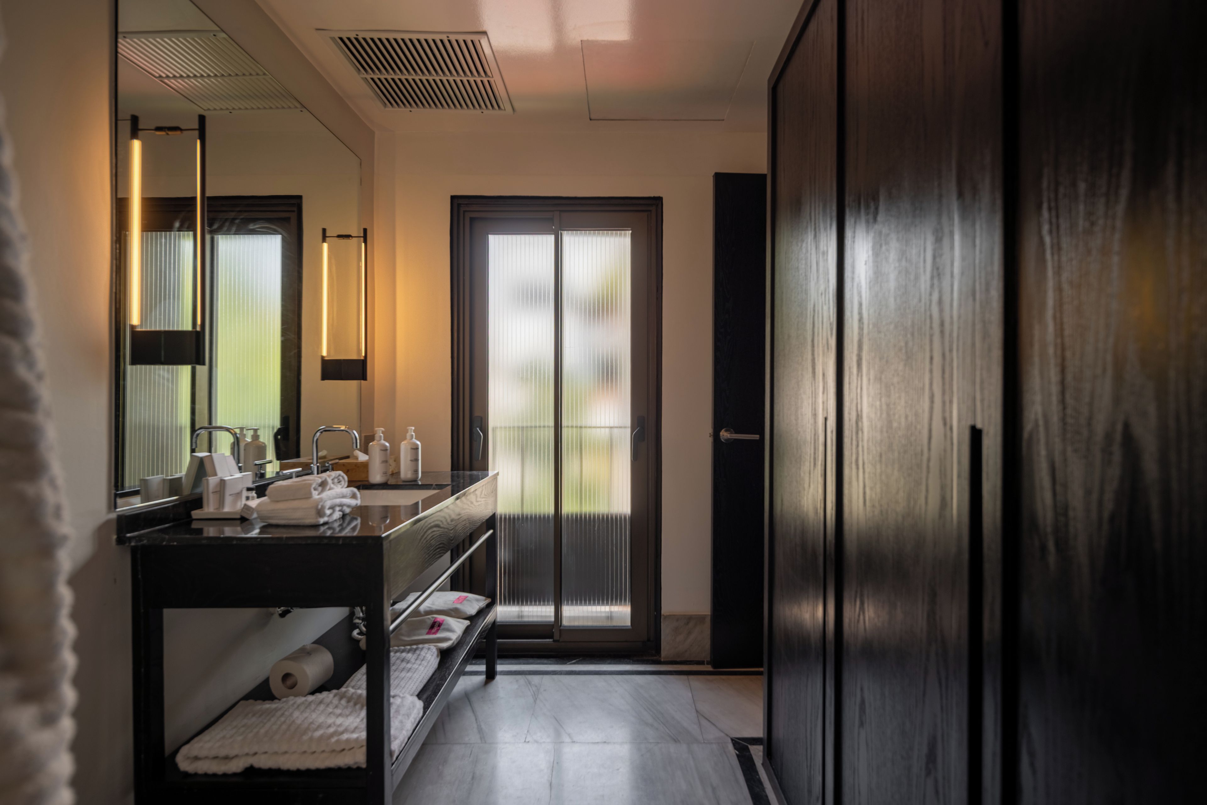A modern bathroom with a dark wood vanity, a large mirror, and a glass door leading to a balcony.