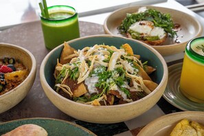 A variety of dishes including nachos, a green smoothie, and a yellow drink on a table. - Hotel Dama (Mexico City)