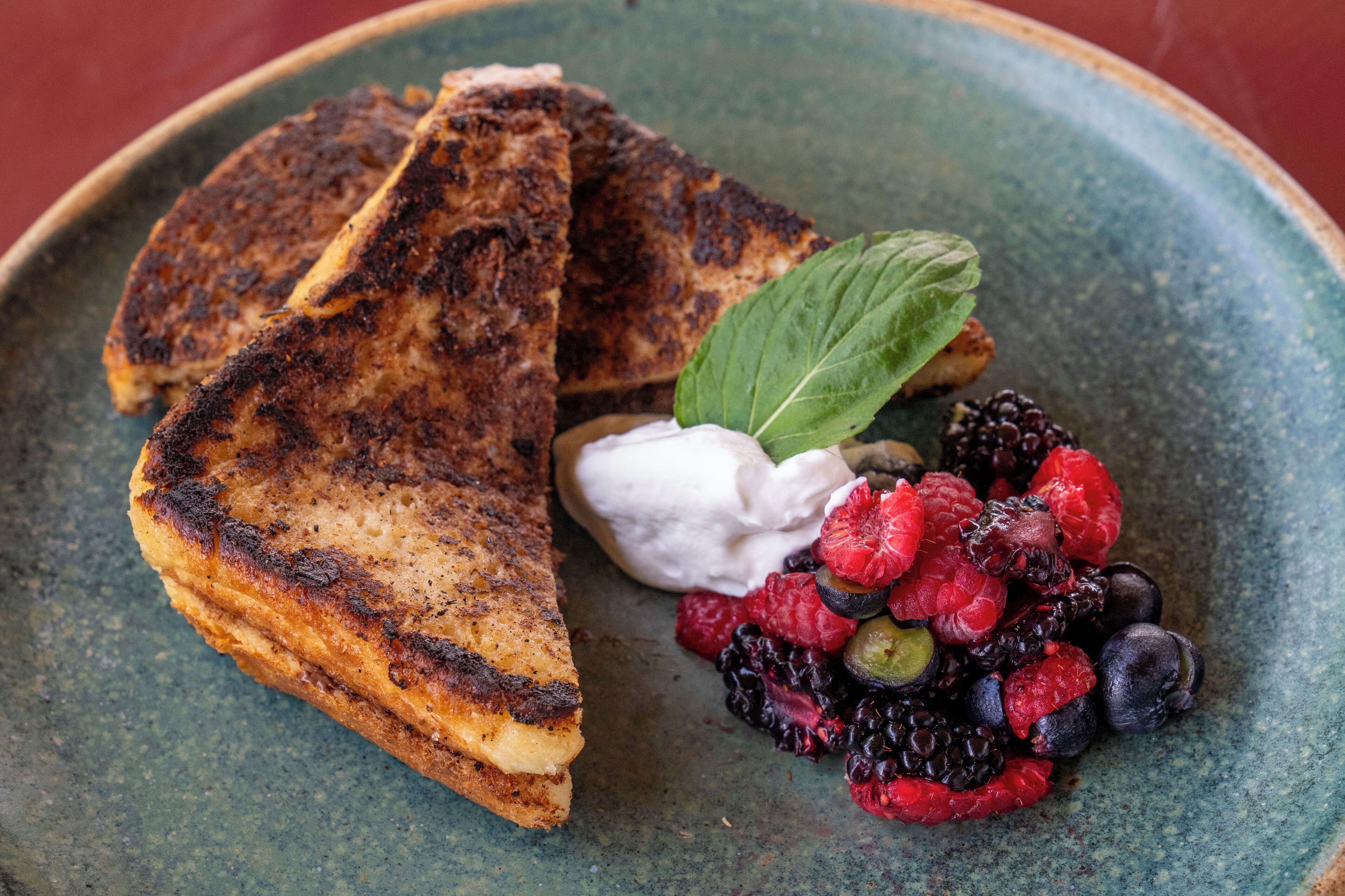 A plate with grilled bread, whipped cream, and mixed berries.