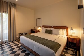 A hotel room with a large bed, a desk, a chair, a nightstand, and a lamp. - Hotel Dama (Mexico City)