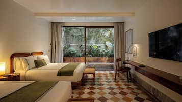 Quarto de hotel com cama, escrivaninha, cadeira, televisão e vista para o verde lá fora.
