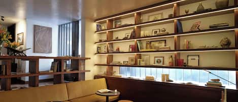 A cozy reading nook with a sofa, two small tables, and a bookshelf filled with books and decorative items.