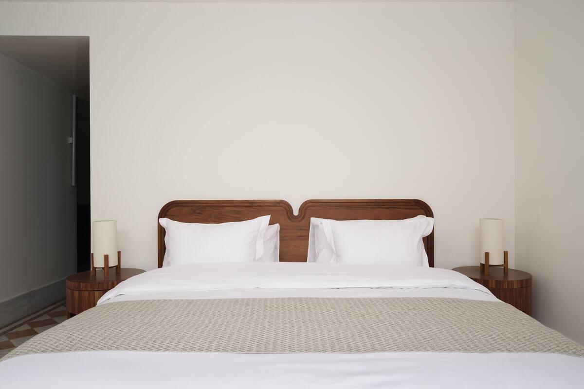A neatly made bed with a wooden headboard, two bedside tables with lamps, and a patterned rug.