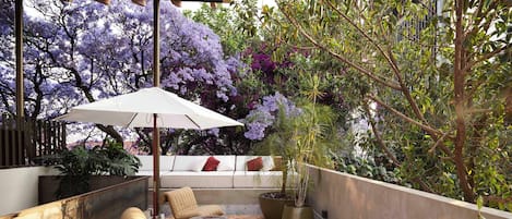 An outdoor seating area with a sofa and chairs, a large umbrella, and potted plants.